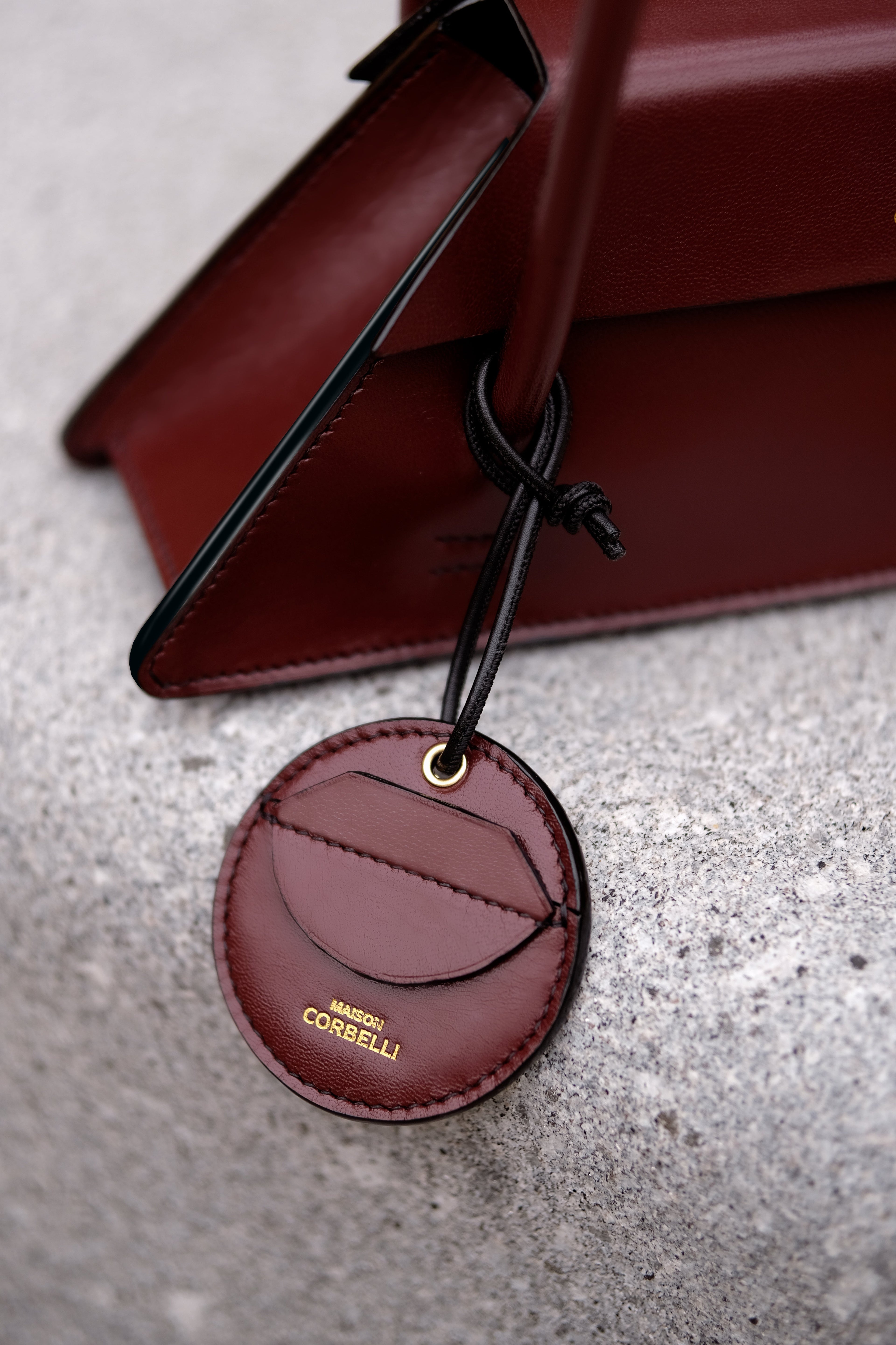 Handbag Elie and accessory Oto from Maison Corbelli collection fixed on the handbag, burgundy colour of both elements on stone bench