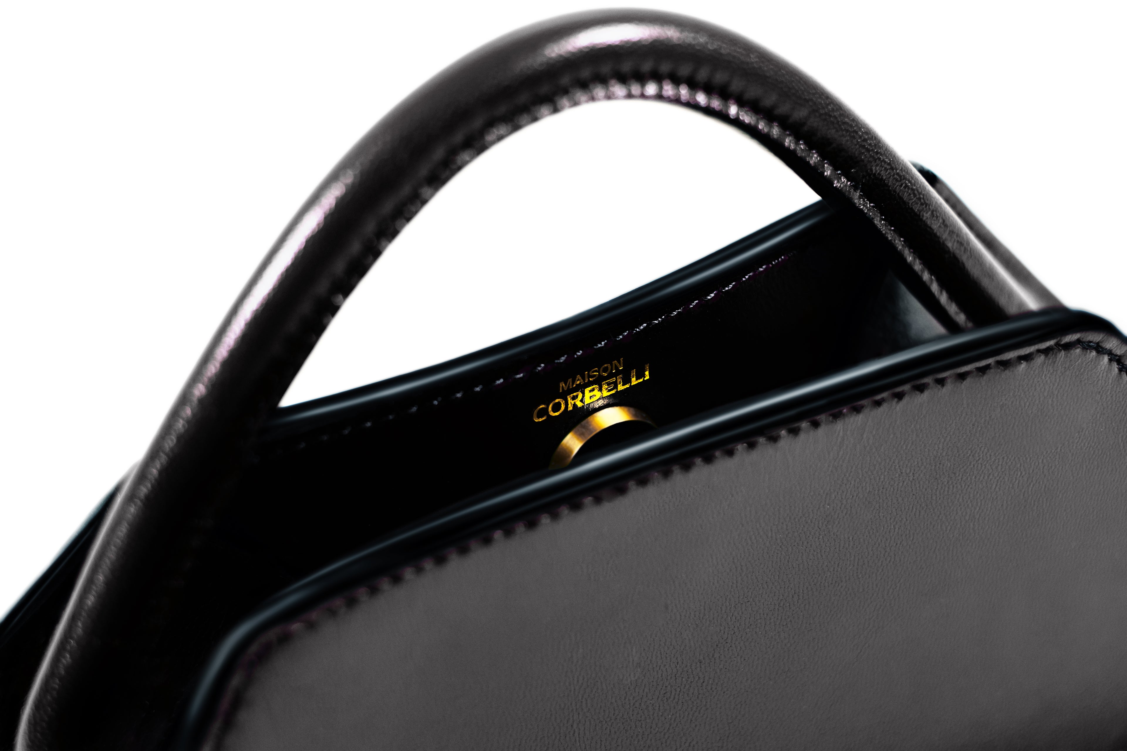 Maison Corbelli Elie mini handbag, black obsidian with golden logo and hardware detail in a Studio with white background, Black, Clutch bag, Hand bag, mediterranean vibe, Premium leather, Unique design, Maison Corbelli, Luxury, Close up. Obsidian Elie Mini Italian calf leather crossbody bag, structured design, Model wearing the Elie Mini structured leather shoulder bag in Obsidian black for lifestyle, Close-up of the gold-toned hardware and calfskin leather texture on the Elie Mini