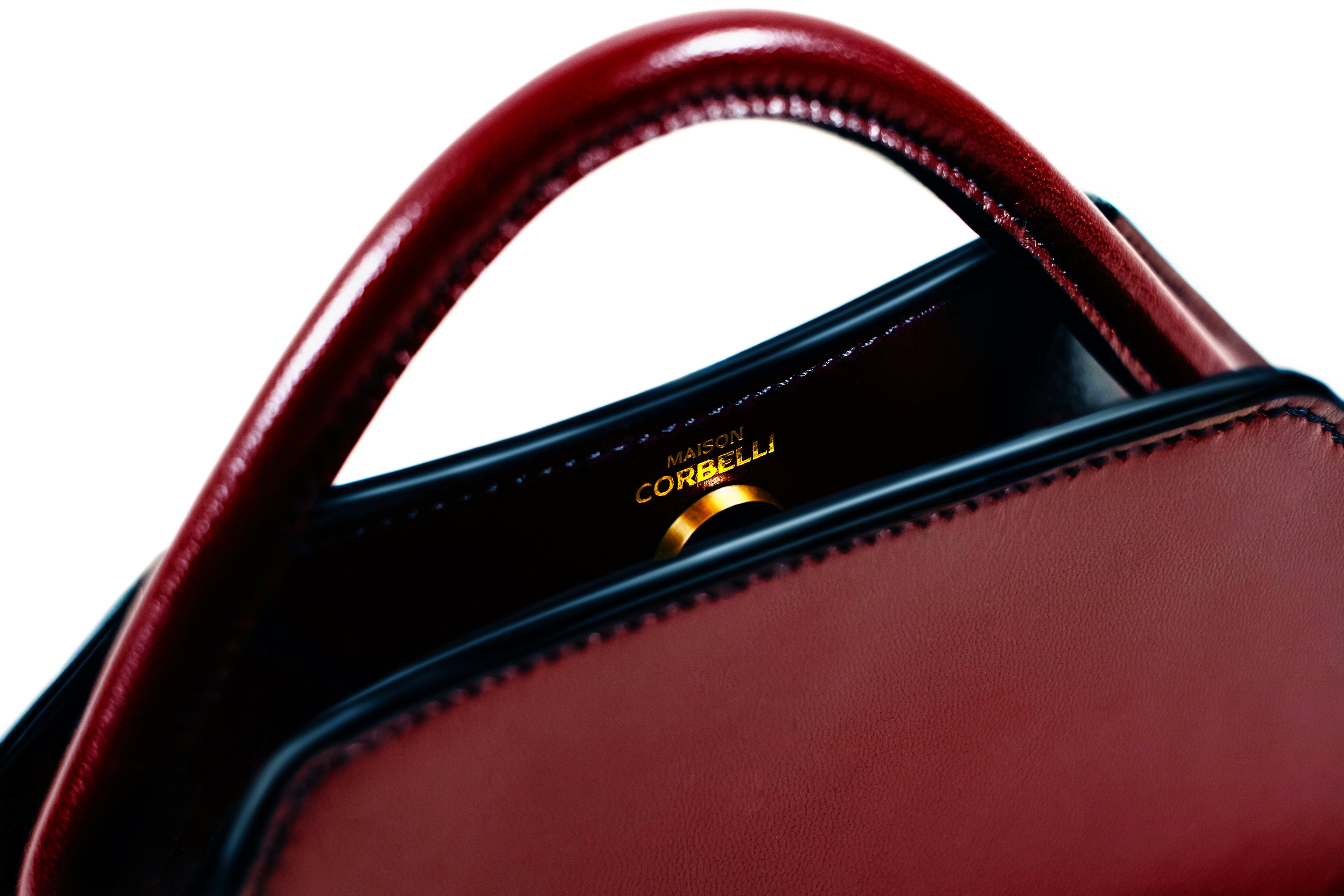 Maison Corbelli Elie mini handbag, burgundy with golden logo and hardware detail in a Studio with white background, Black, Clutch bag, Hand bag, mediterranean vibe, Premium leather, Unique design, Maison Corbelli, Luxury, Close up.