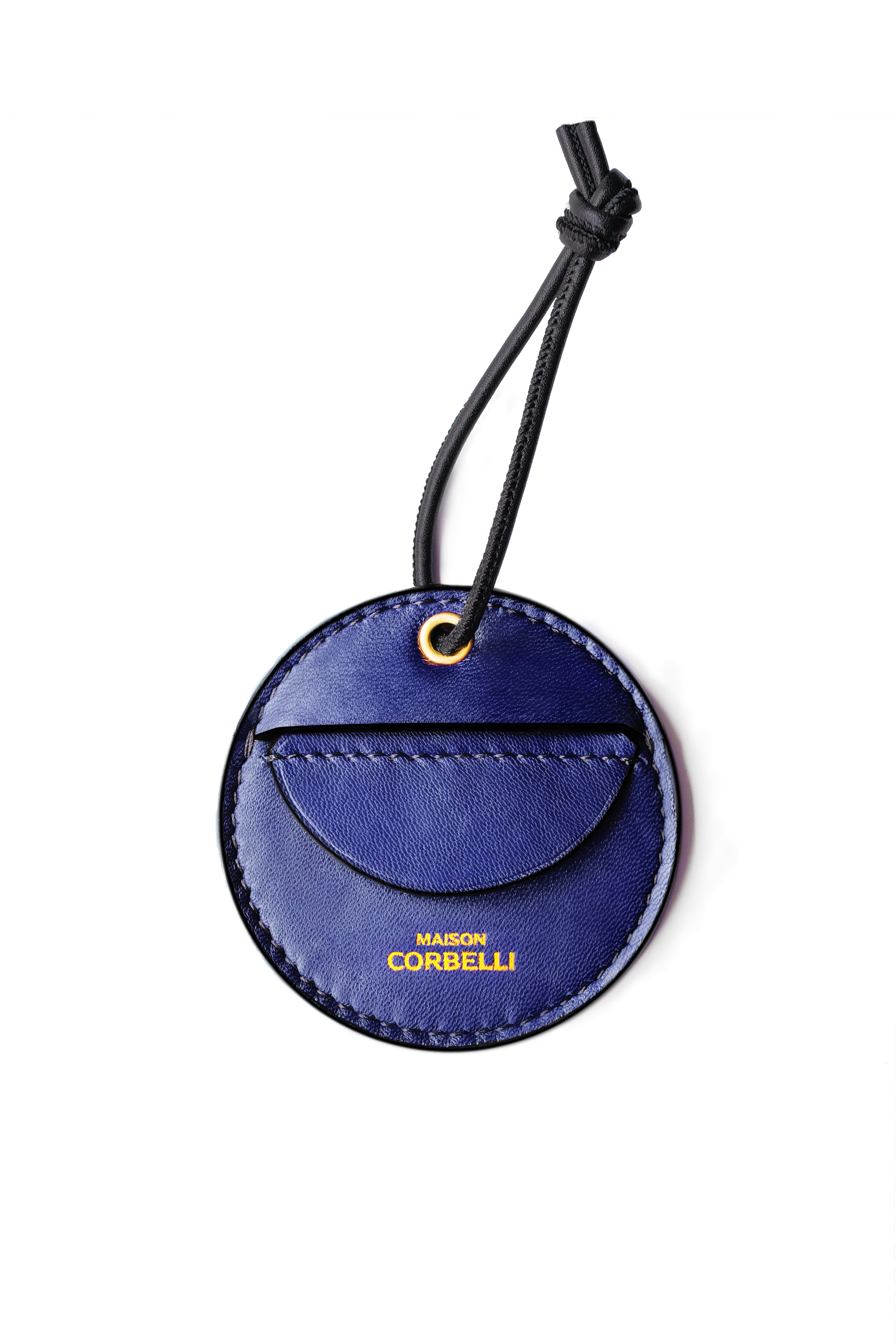 Blue leather luggage tag with 'MAISON CORBELLI' branding on a white background, Round leather tag with a hand holding it on a white background, Oto, coin holder, Navy blue, Blue, dark blue, gift for christmas, present, gold-colored accessories, coin purse, a finger holds it, Front view, Model, Studio, Burgundy, bag, mediterranean vibe, Premium leather, Unique design